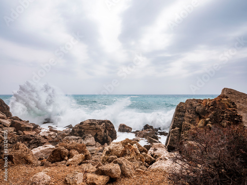 Waves hitting rocks on the Baunei coast. Background blur and with sunlight filtering from the clouds. Dramatic natural background.