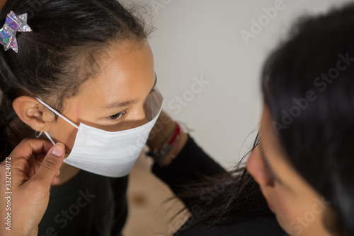 Schilderij op canvas Latin mother puts the mask on her daughter, worried face tries to prevent the spread