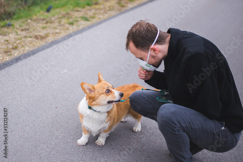 a man on a walk with a corgi dog wearing a face mask and during coronavirus pandemia photo