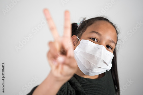 Portrait of girl with prevention mask who smiles and shows the sign of v in victory and hope against the coronavirus infection. Covid 19 hope concept.