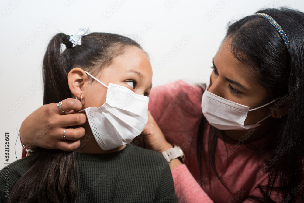 Mother cares for and puts the medical mask on her daughter to prevent illness. Woman wears a smart watch. Little girl looks to her mother. Concept of contagion of the coronavirus, COVID-19.