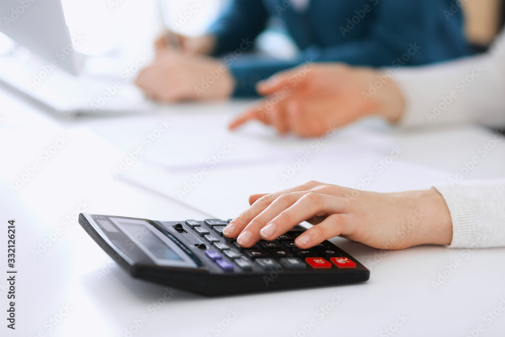 Accountant checking financial statement or counting by calculator income for tax form, hands closeup. Business woman sitting and working with colleague at the desk in office. Tax and Audit concept Accountant checking financial statement or counting by calculator income for tax form, hands closeup. Business woman sitting and working with colleague at the desk in office. Tax and Audit concept