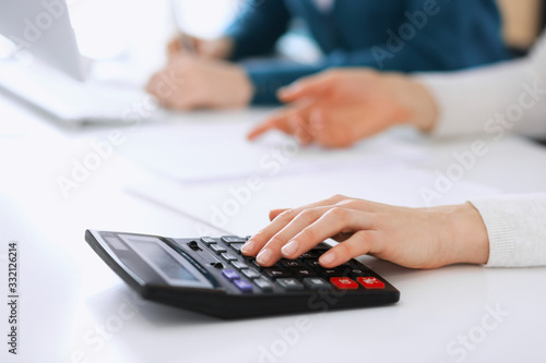 Accountant checking financial statement or counting by calculator income for tax form, hands closeup. Business woman sitting and working with colleague at the desk in office. Tax and Audit concept © Iryna
