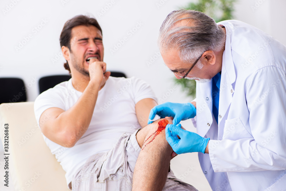 Leg injured man visiting old doctor in first aid concept Leg injured man visiting old doctor in first aid concept