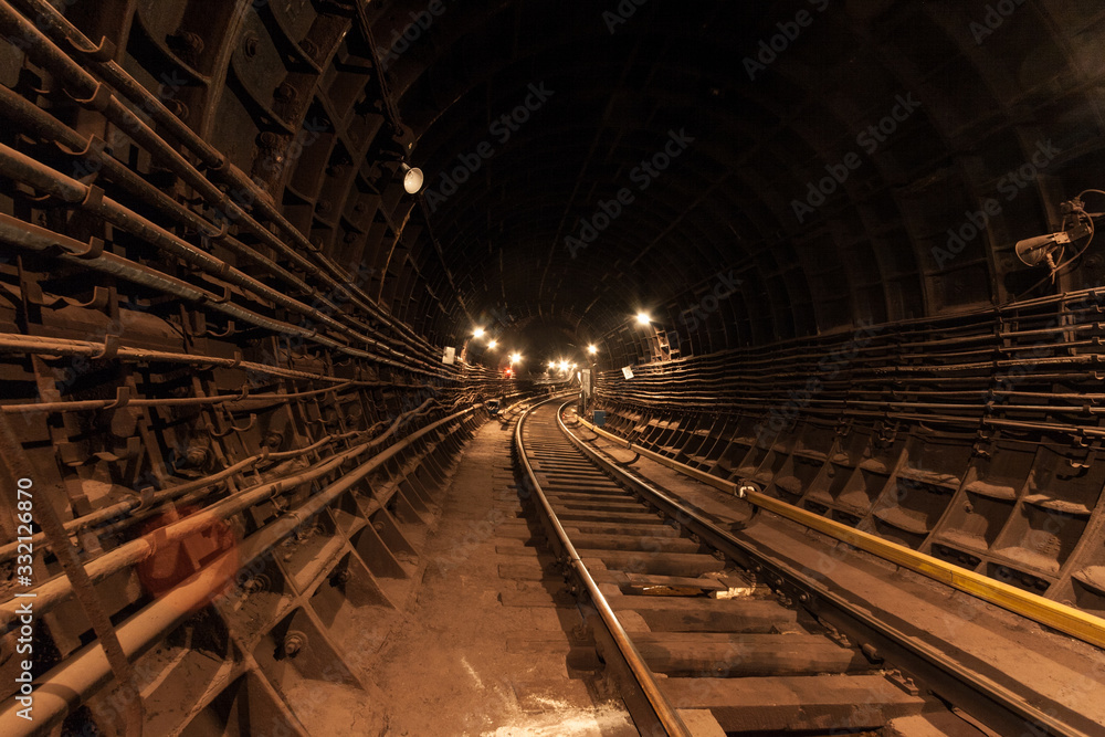 Obraz premium A lighted reinforced concrete subway tunnel, cable routes are laid, the railroad tracks turn left. In front of them are iron vertical boxes of automatics.