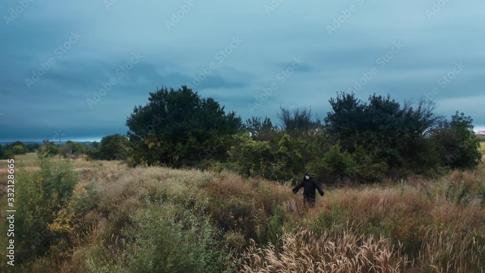 Mysterious ghost in black cloak among nature. Dark figure standing on the field under cloudy sky. Scary death. Horror concept. Drone view. Mysterious ghost in black cloak among nature. Dark figure standing on the field under cloudy sky. Scary death. Horror concept. Drone view.