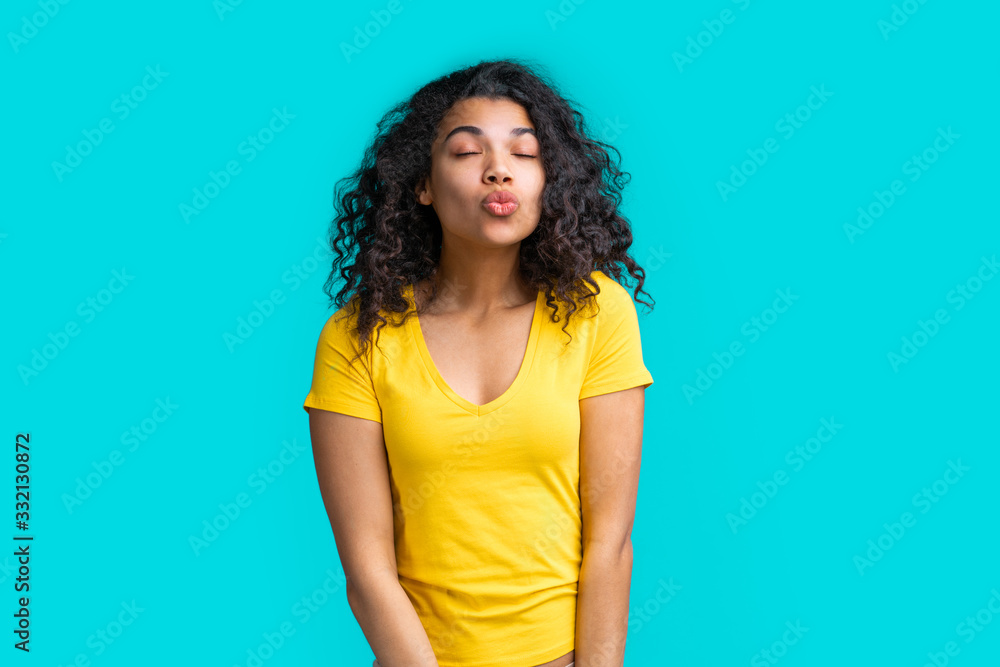 Portrait of beautiful smiling dark skinned girl wearing bright colored yellow t-shirt isolated over blue background Portrait of beautiful smiling dark skinned girl wearing bright colored yellow t-shirt isolated over blue background
