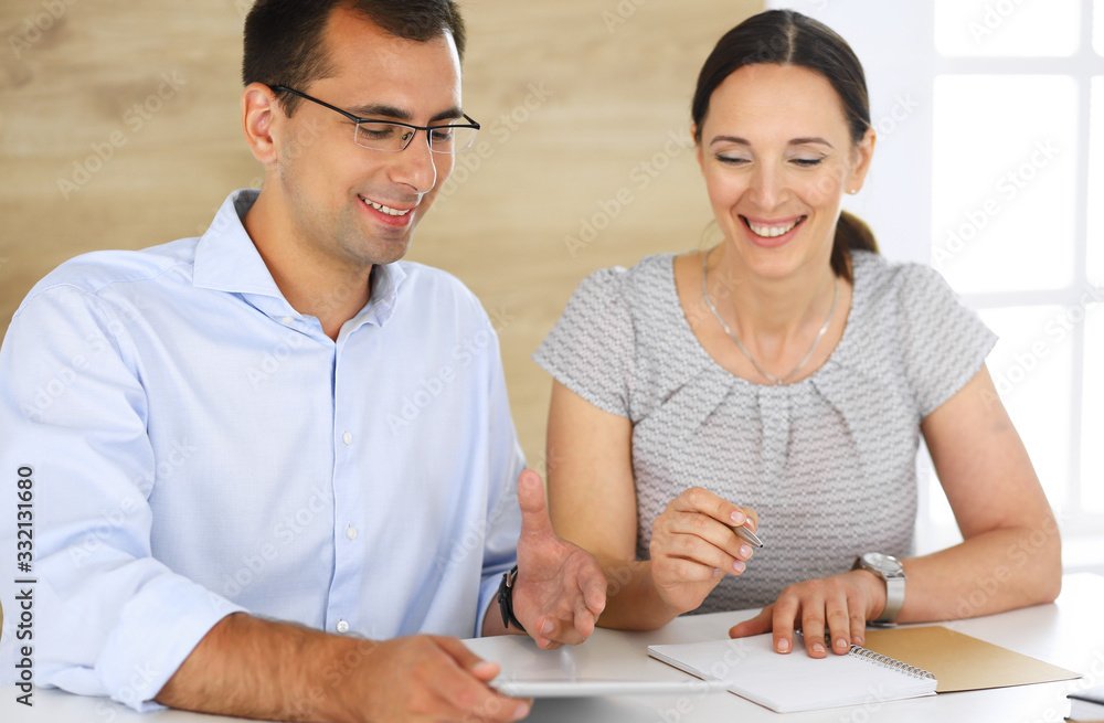 Businessman and hispanic businesswoman using tablet computer in modern office. Headshot of entrepreneur at meeting. Group of diverse people. Teamwork, partnership and business concept Businessman and hispanic businesswoman using tablet computer in modern office. Headshot of entrepreneur at meeting. Group of diverse people. Teamwork, partnership and business concept