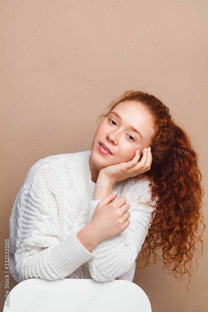 beautiful red-haired girl in a white sweater smiles and looks at the camera on a beige background in the studio beautiful red-haired girl in a white sweater smiles and looks at the camera on a beige background in the studio