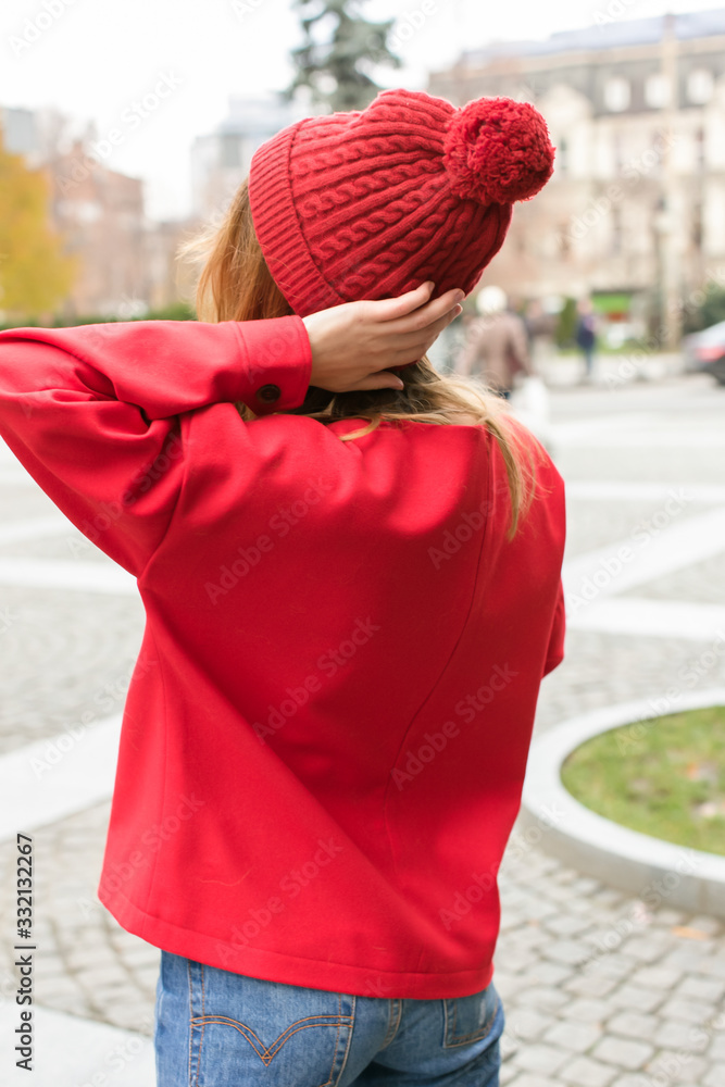 European girl in knitted red sweater and hat stands on street with paper cup takeaway coffee. Coffee break