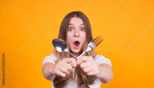 Surprised girl holds cross fork and spoon in her hands. © Svitlana