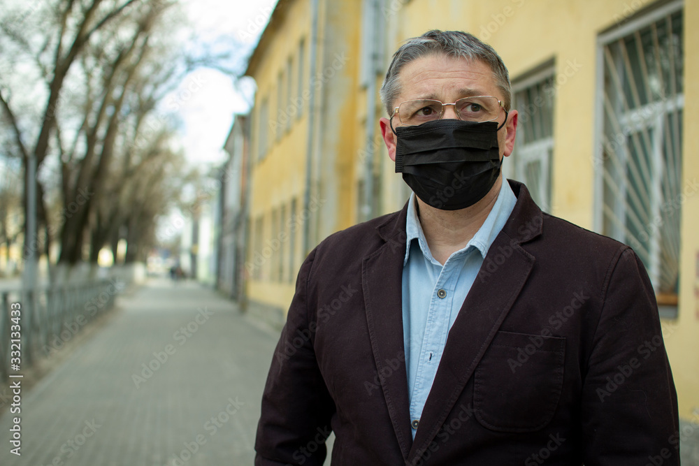 A middle- aged European in a protective disposable black medical mask in the city. A middle- aged European in a protective disposable black medical mask in the city.