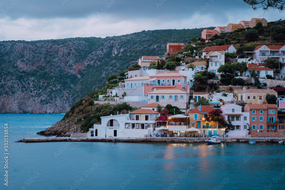 Assos town in evening twilight. Vivid colorful local house buildings at hill. Kefalonia, Greece
