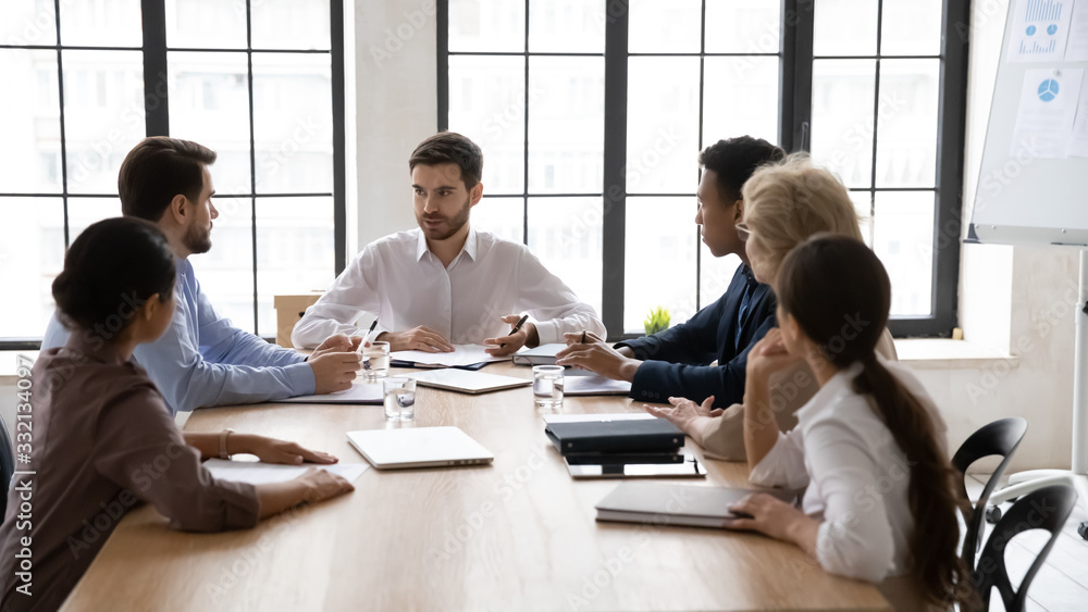 Serious multiracial businesspeople gather at desk in office discuss business ideas together, focused male team leader hold meeting with diverse coworkers in boardroom, cooperation concept Serious multiracial businesspeople gather at desk in office discuss business ideas together, focused male team leader hold meeting with diverse coworkers in boardroom, cooperation concept