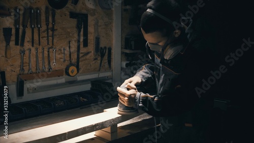 Man polishing solid wood, joiner labouring in mask for safety
