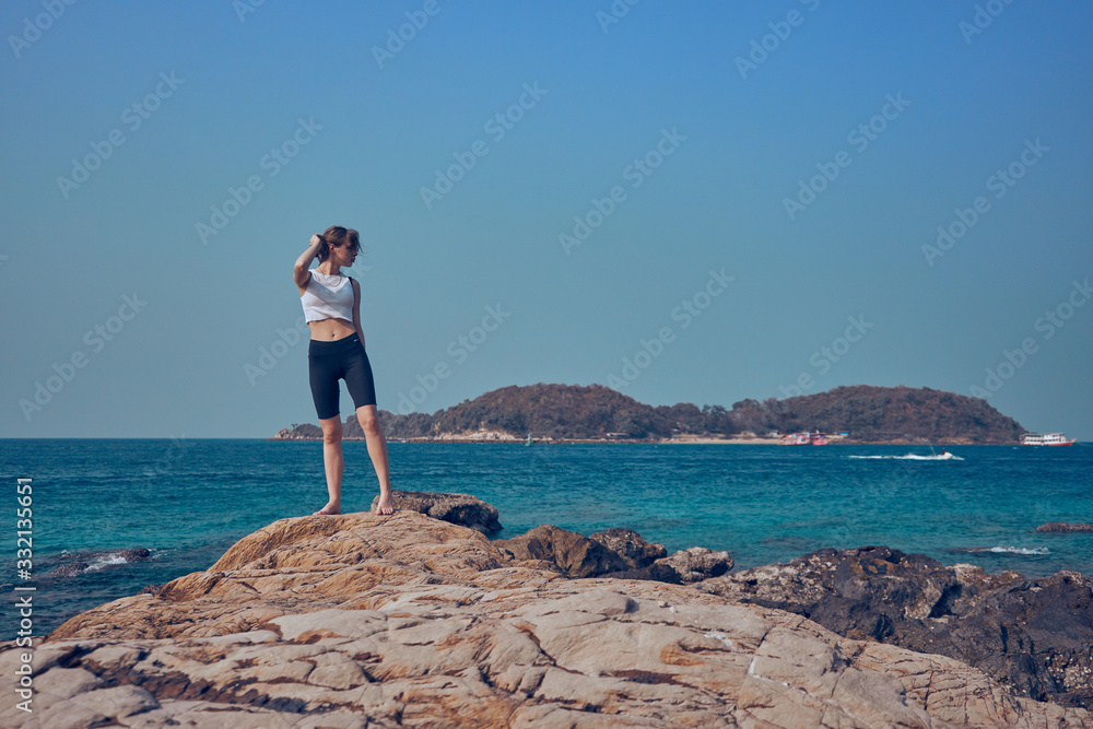 Girl model against the sea and ocean in peas and on stones in shorts and swimsuit in Thailand 