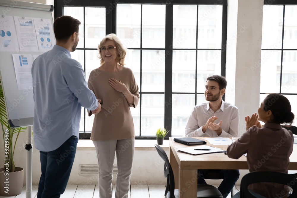 Male team leader handshake middle-aged female employee greeting with promotion at meeting in office, happy businessman shake hand of excited woman worker congratulate with job achievements Male team leader handshake middle-aged female employee greeting with promotion at meeting in office, happy businessman shake hand of excited woman worker congratulate with job achievements
