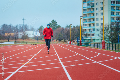 Runner wearing medical mask, Coronavirus pandemic Covid-19 in Europe. Sport, Active life in quarantine surgical sterilizing face mask protection. Outdoor run on athletics track in Corona Outbreak