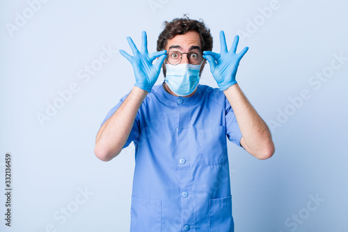 young man feeling shocked, amazed and surprised, holding glasses with astonished, disbelieving look. coronavirus concept photo