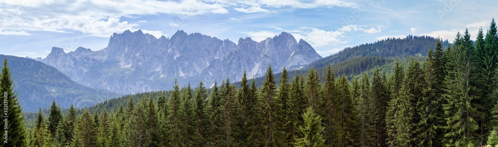 Famous Gosaukamm in Upper Austria. Seen here in beautiful sunny summer weather with some clouds in the blue sky. Green pine trees are all over the mountains in front. Famous Gosaukamm in Upper Austria. Seen here in beautiful sunny summer weather with some clouds in the blue sky. Green pine trees are all over the mountains in front.
