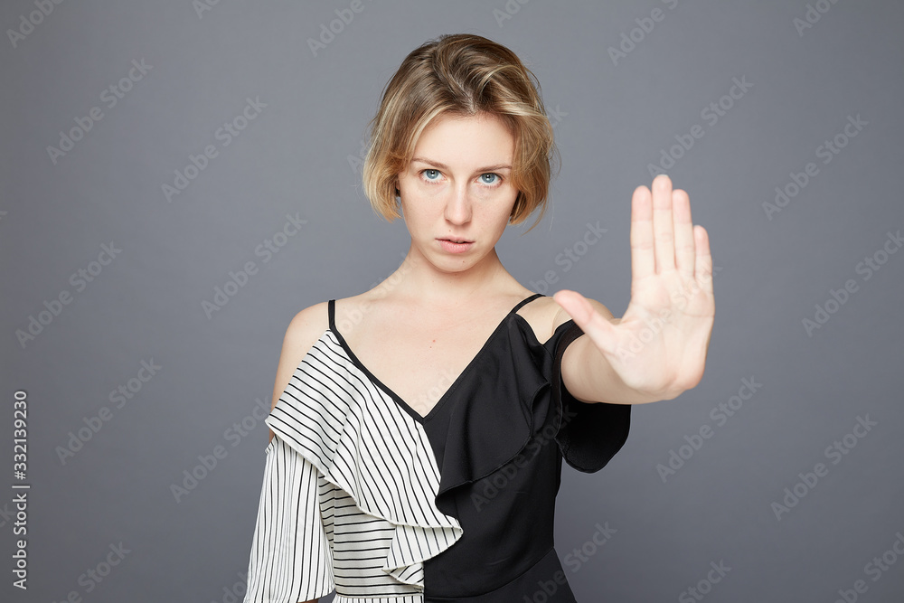 Studio portrait of grumpy young female with irritated expression, makes stop gesture and keeps palms in front, asks to stop panic and be quiet, stands against grey background. Body language concept. Studio portrait of grumpy young female with irritated expression, makes stop gesture and keeps palms in front, asks to stop panic and be quiet, stands against grey background. Body language concept.