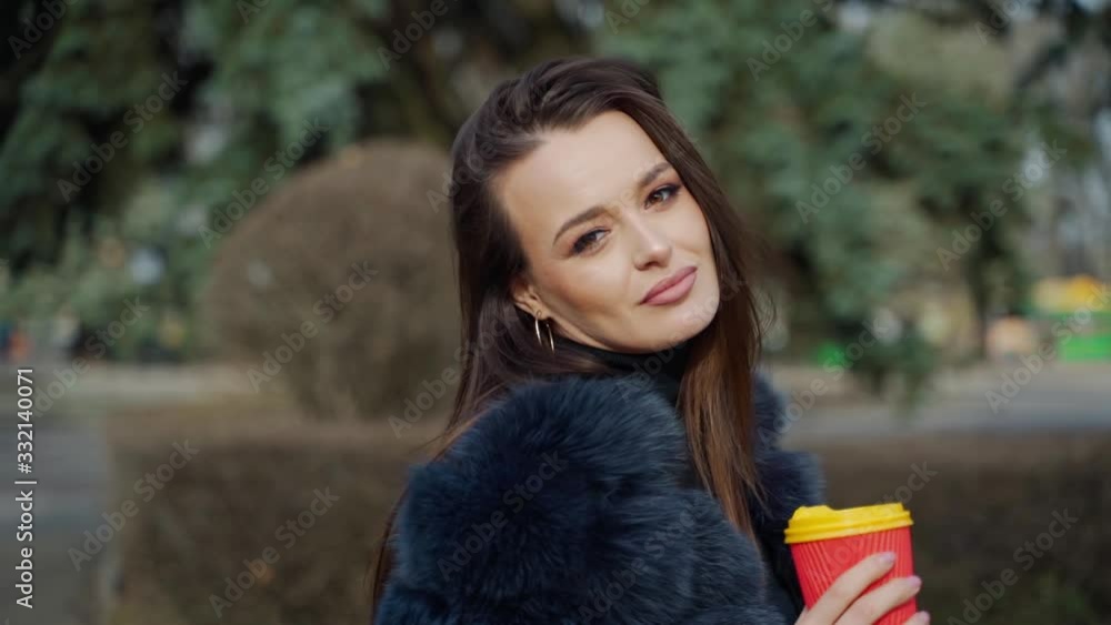 Face of a luxury young woman. Portrait of attractive model with long dark hair in warm coat holding a plastic cup of coffee and looking at camera in the park. Face of a luxury young woman. Portrait of attractive model with long dark hair in warm coat holding a plastic cup of coffee and looking at camera in the park.