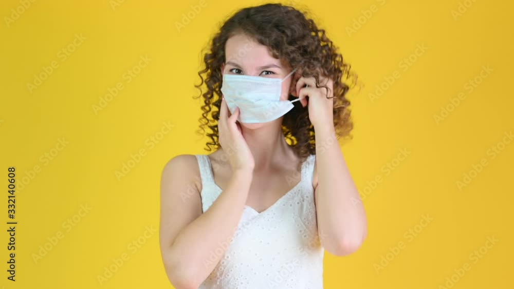 A young girl puts on a medical mask. Isolated on a yellow background. health care and medical concept. A young girl puts on a medical mask. Isolated on a yellow background. health care and medical concept.