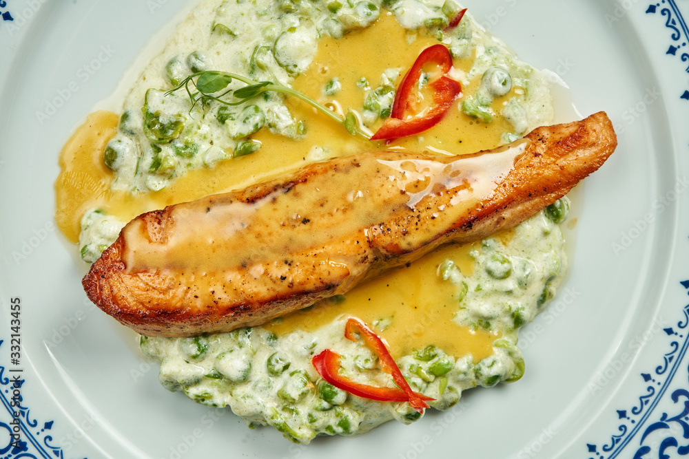 Delicious grilled salmon steak filet with peas in a creamy sauce in a white plate on a wooden background. Tasty seafood