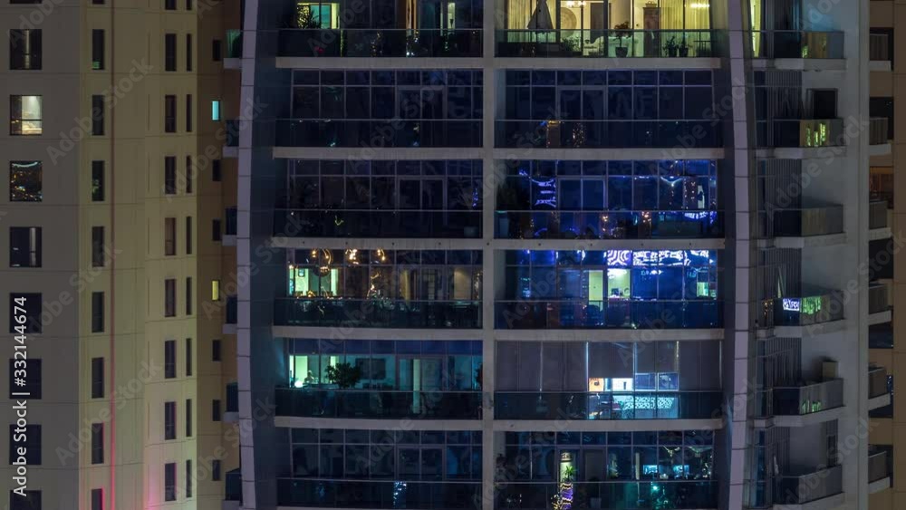 Rows of glowing windows with people in the interior of apartment building with balconies at night. Modern skyscraper with glass surface. Concept for business and modern life. Zoom in Rows of glowing windows with people in the interior of apartment building with balconies at night. Modern skyscraper with glass surface. Concept for business and modern life. Zoom in