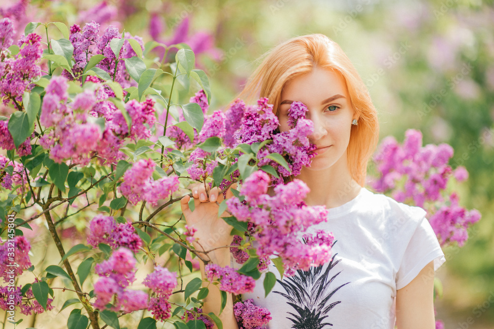 Handsome woman with red hair and pretty smile posing in lilac garden with flowers and enjoys the smell Handsome woman with red hair and pretty smile posing in lilac garden with flowers and enjoys the smell
