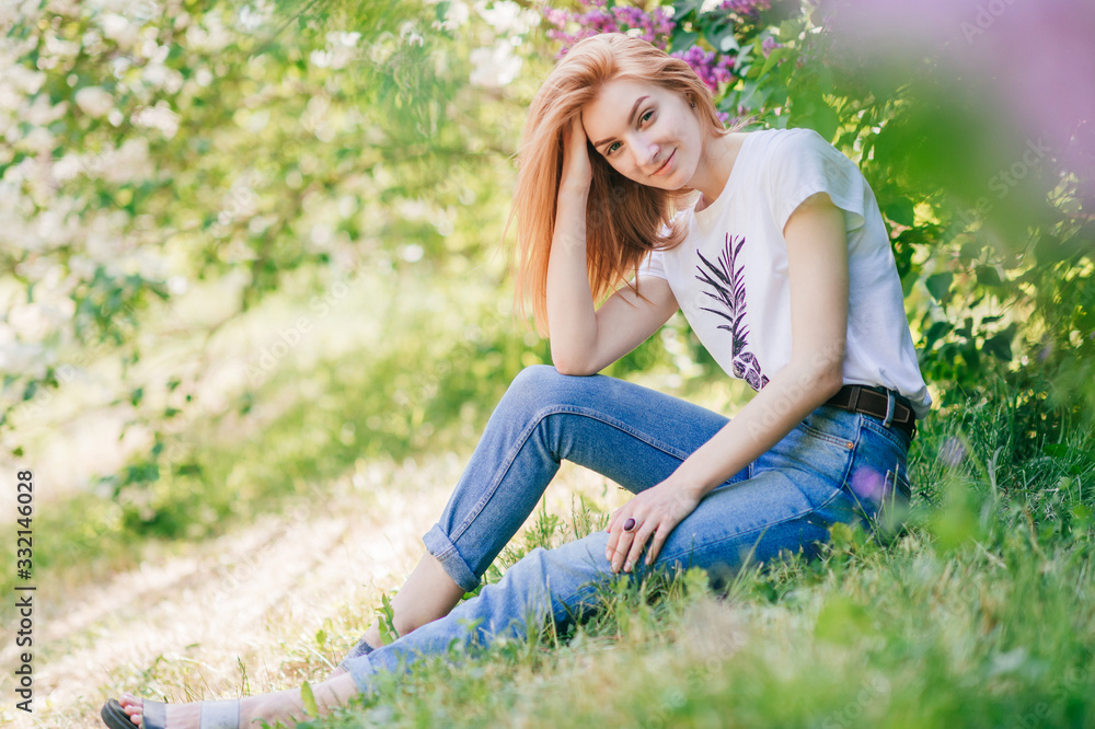 Portrait of emotional red-hair girl sits in a lilac garden Portrait of emotional red-hair girl sits in a lilac garden