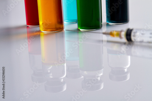 Medicine vials reflecting on white surface. Macro shot of syringe and bottles.