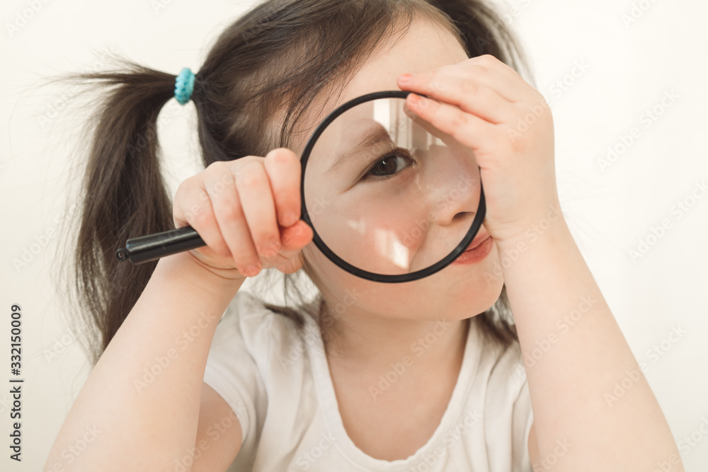 Little girl plays a detective. A child examines something through a magnifying glass. A girl with two ponytails plays cute. Toddler indulges with a magnifier Little girl plays a detective. A child examines something through a magnifying glass. A girl with two ponytails plays cute. Toddler indulges with a magnifier