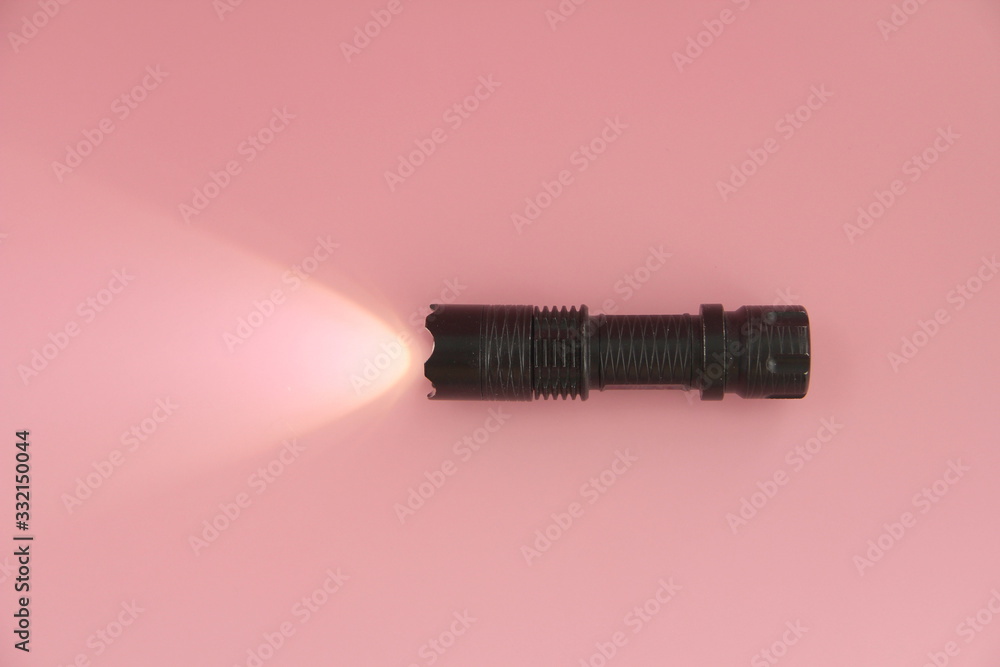 The black turned on electric manual lamp lies on a pink background. Light from a lantern on the surface The black turned on electric manual lamp lies on a pink background. Light from a lantern on the surface
