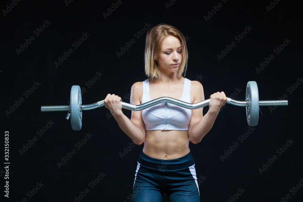 Obraz premium Close-up portrait of a fitness Muscular young girl posing with curly barbell at the gym isolated on a black background