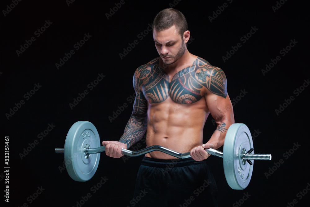 Tattooed strong muscular athletic man pumping up muscles with barbell on black background Tattooed strong muscular athletic man pumping up muscles with barbell on black background