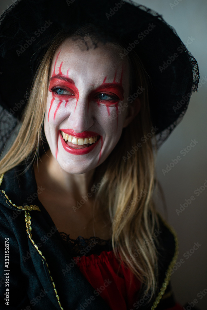 Portrait of a mysterious girl with fair hair as a witch with bright make-up and leaking lipstick mysteriously looks to the side with wide smile Portrait of a mysterious girl with fair hair as a witch with bright make-up and leaking lipstick mysteriously looks to the side with wide smile