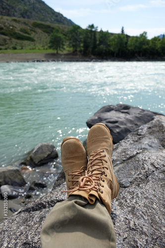 Woman's legs in light brown boots sitting on the edge near river.