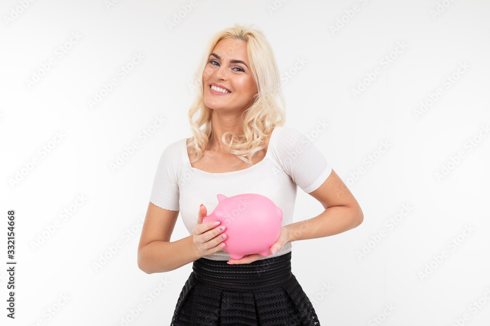 smiling beautiful girl in black and white clothes with a piggy bank in hands on a white background with copy space