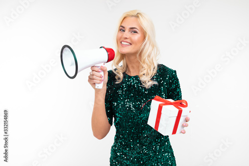 joyful girl in a dress announces gifts in a megaphone holding a gift box on a white studio background