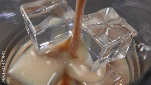 Irish cream liqueur is poured into a glass with ice cubes. Macro shot. Alcoholic drinks at the bar.