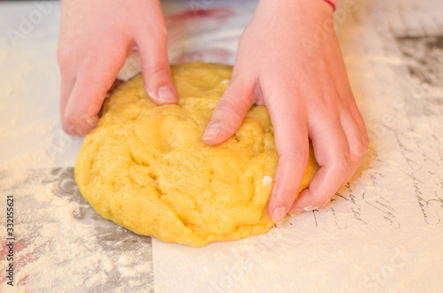 Female hands knead the dough for a sweet cake on a table sprinkled with flour. Making shortcrust pastry at home in the kitchen. Selective focus.