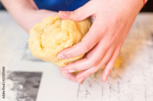 Female hands knead the dough for a sweet cake on a table sprinkled with flour. Making shortcrust pastry at home in the kitchen. Selective focus.