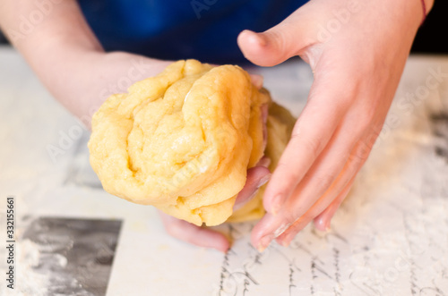 Female hands knead the dough for a sweet cake on a table sprinkled with flour. Making shortcrust pastry at home in the kitchen. Selective focus.