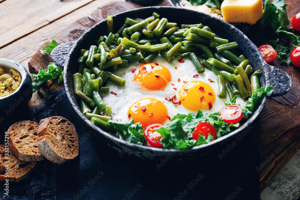 Pan of fresh fried eggs with tomatoes, green beans, bread, spices and herbs on rustic wooden background Pan of fresh fried eggs with tomatoes, green beans, bread, spices and herbs on rustic wooden background
