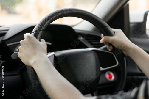 Female hands on the steering wheel of a car while driving. Against the background, the windshield and road,Close-up of a woman's hand driving a car © sek_gt