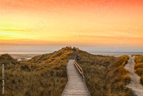 Fototapeta Naklejka Na Ścianę i Meble -  Wooden path and stairs crossing the dunes to the beach of Norddorf, Amrum, in sunset