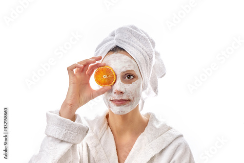 Beautiful woman with a white cosmetic mask on her face and slices of oranges in her hand.