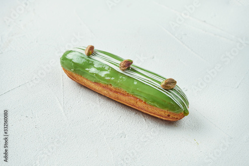 Beautiful and tasty eclair with white-red glaze and pistachio flavor on a white texture background. Close up