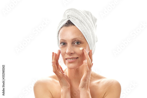 A young woman cares for her face and smears cream. White isolated background.